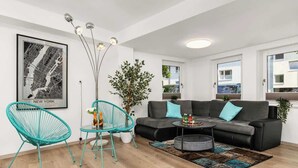 A modern living room with a black leather sofa, teal chairs, a coffee table, and a framed cityscape poster. - Mola Apartments-Wetter/ 5 P/Parking/Terrasse/Grill (Wetter (Ruhr))