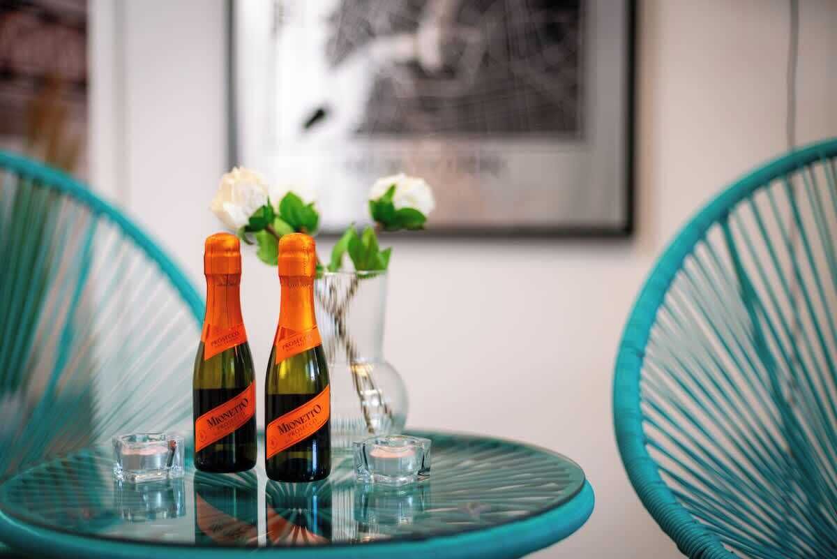 Dos botellas de vino Monnetto sobre una mesa de cristal con un florero de flores blancas al fondo.