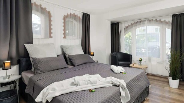 A modern hotel room with a large bed, a bedside table with a lamp, a chair, a small table with a vase, and a potted plant. - Mola Apartments-Wetter/ 5 P/Parking/Terrasse/Grill (Wetter (Ruhr))