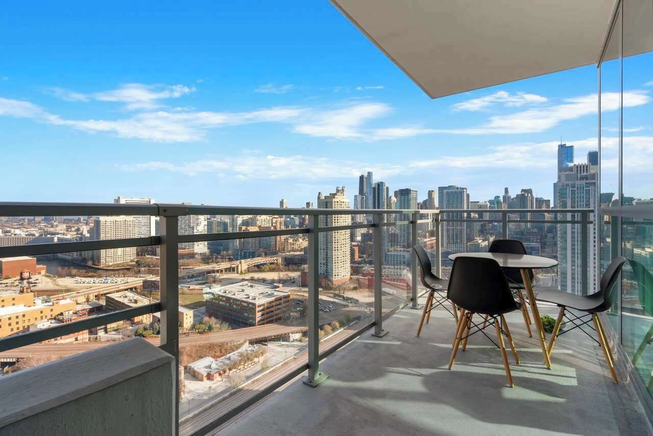 A high-rise balcony with a city view, featuring a table and chairs.