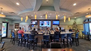 A bar area with multiple screens, a Christmas tree, and bar stools. - Orlando resort champions gate 10 min to Disney  (Four Corners)