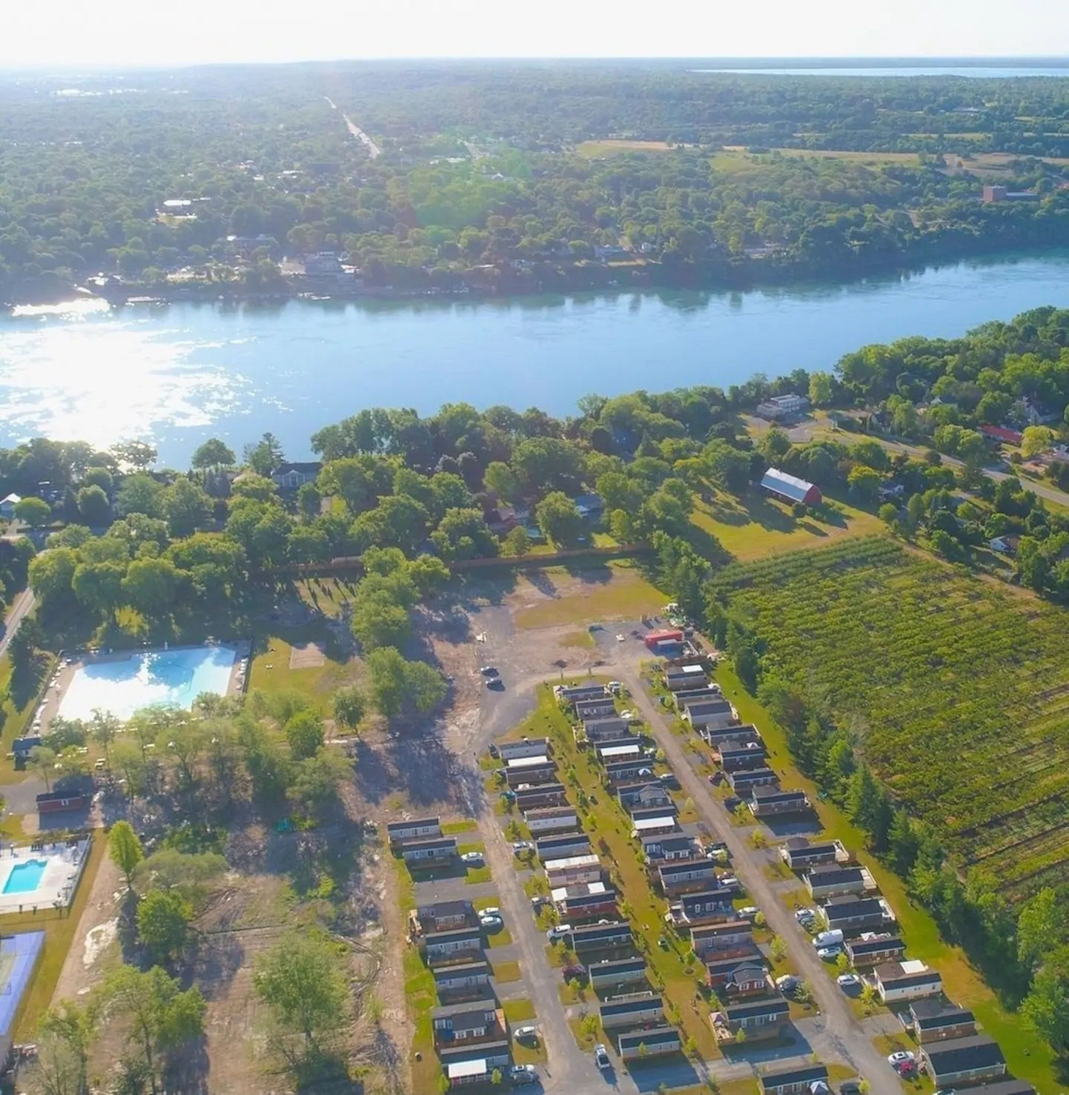 An aerial view of a residential area with a large body of water, a swimming pool, and a row of houses.