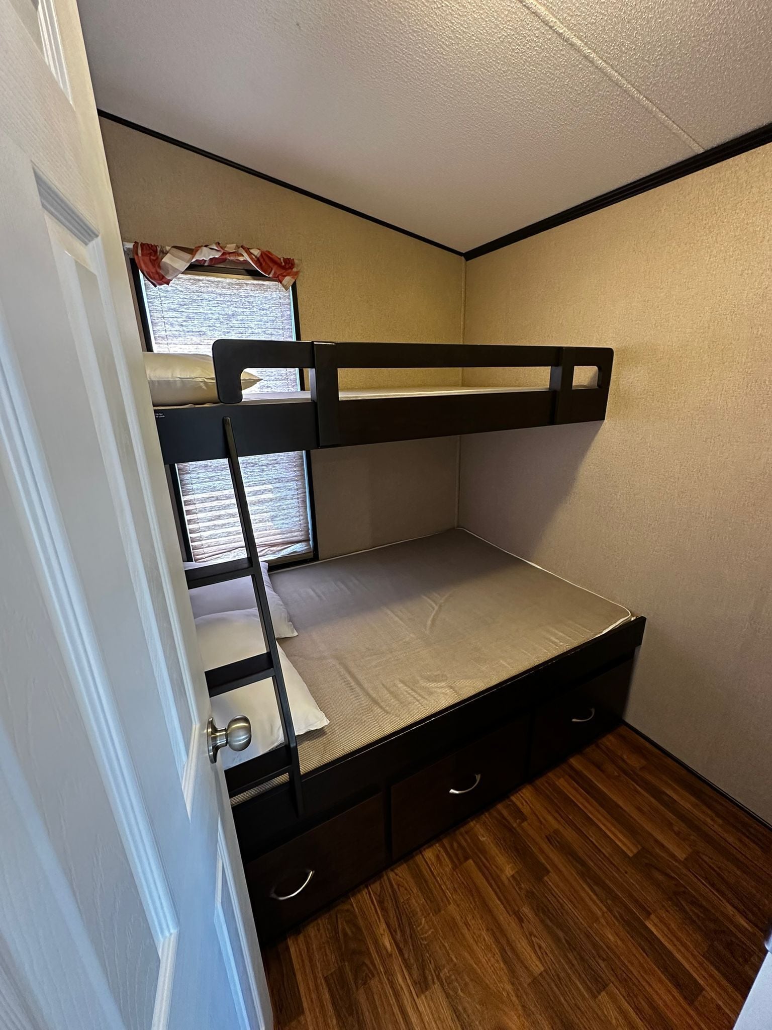 A bunk bed room with a window, wooden flooring, and a door.