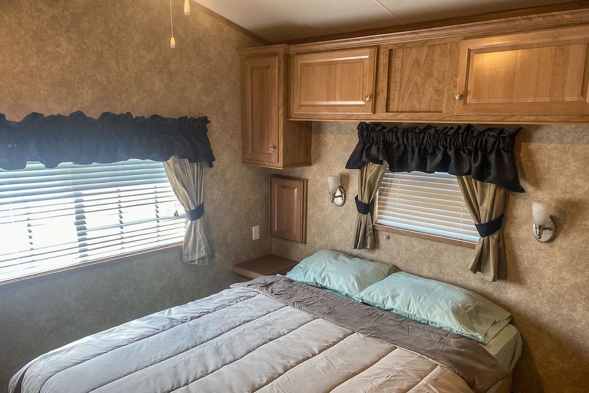 A bedroom with a bed, curtains, a window, and wooden cabinets.