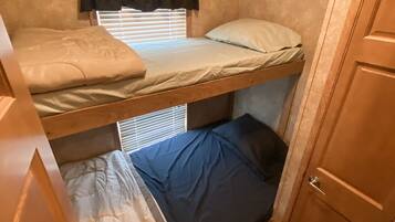 A compact RV interior with a bunk bed, a small window with blinds, and a wooden door.