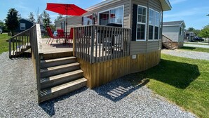A wooden deck with a staircase leading to a small building with a red umbrella and a number 207 sign. - Falcon Cottages (Niagara-on-the-Lake)