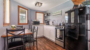 Una cocina compacta con gabinetes blancos, un refrigerador negro, una estufa y un microondas.