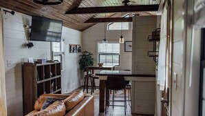 Ein gemütliches Interieur mit Holzboden, einem Ledersofa, einem Essbereich und einer Küche mit weißen Wänden und Holzbalken.