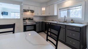 A modern kitchen with white cabinetry, a marble countertop, and a window providing natural light.