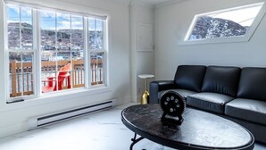 A modern living room with a black leather sofa, a round coffee table with a gear decoration, and a view of a snowy landscape through large windows.