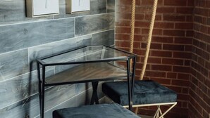 A modern interior with a glass-top table, dark blue cushioned seating, and framed artwork on a grey-tiled wall. - Stylish Queen Suite Near SIU Carbondale (Carbondale)