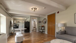 A modern living room with a grey sofa, a round coffee table, and a white ottoman. There is a kitchen area in the background with a dining table and chairs. - Stylish Queen Suite Near SIU Carbondale (Carbondale)