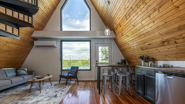 Un espacio habitable estilo loft con cocina, techo de madera, ventanas amplias y vista a zonas verdes.