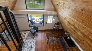 Un espacio tipo loft con un tragaluz grande, paredes de madera, una zona de comedor con mesa y sillas, y vista a un lago.