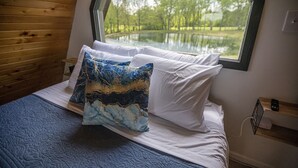 Un dormitorio con un ventanal grande, una cama con ropa de cama blanca y azul, y un cabecero de madera.