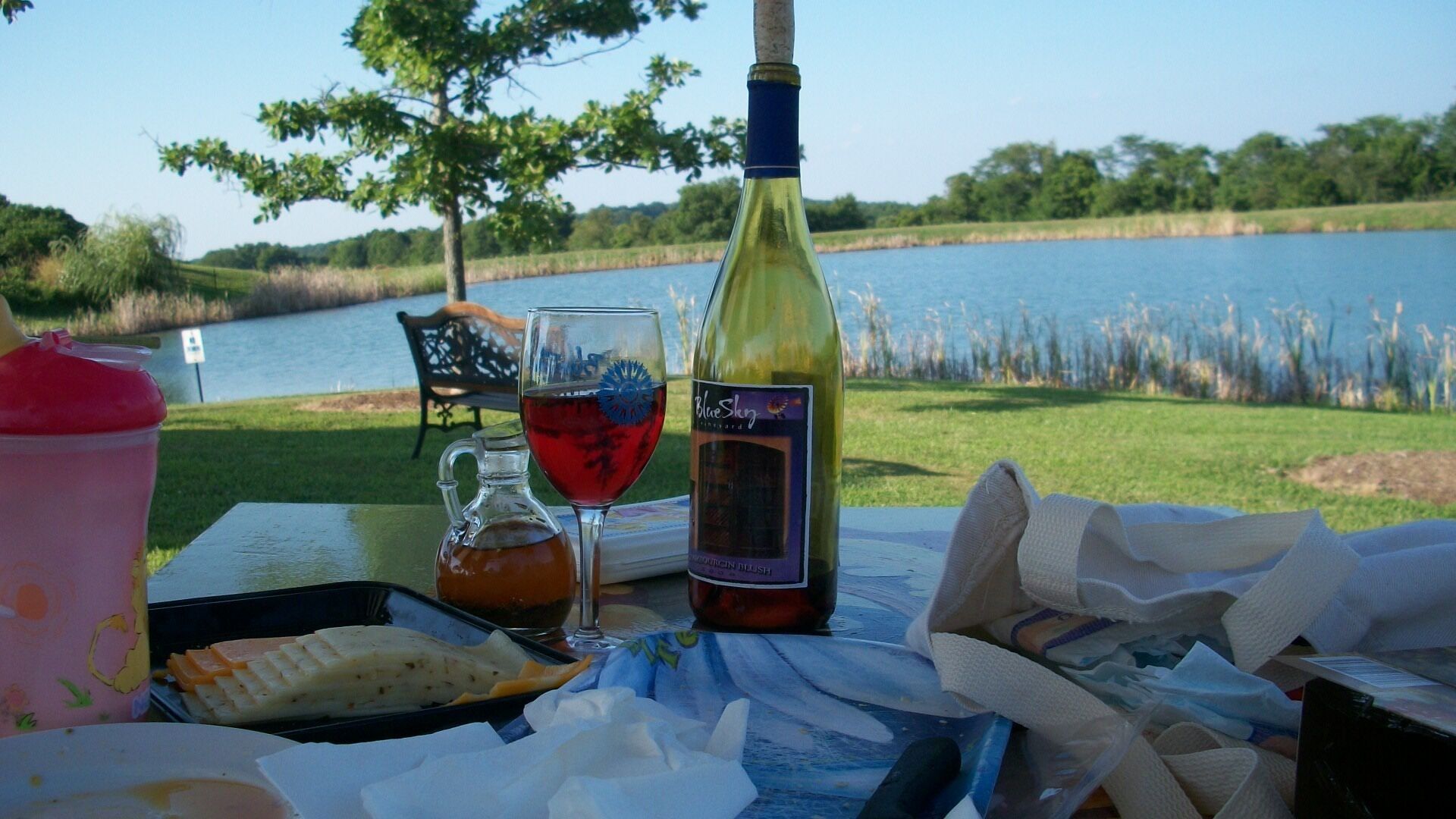 A table with a bottle of wine, a glass of red wine, a pitcher, and a tray with food.