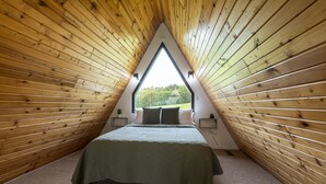 A triangular room with wooden walls and a bed with a green bedspread. - 2BR A-Frame Cabin w/ Hot Tub Near Wine Trail (Makanda)