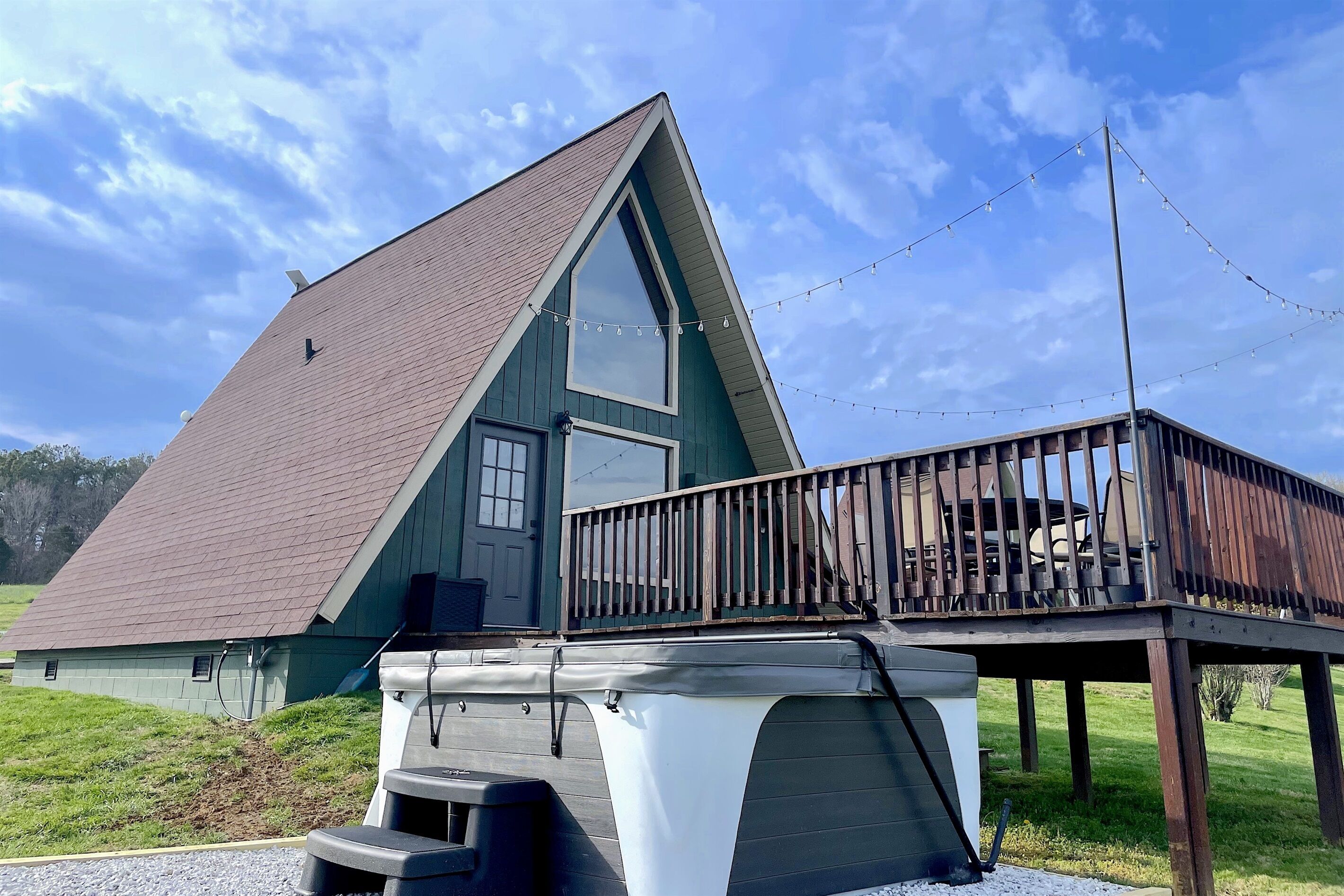 A house with a steeply pitched roof, a large window, and a wooden deck with a hot tub.