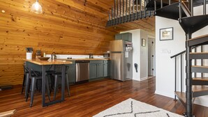A kitchen with wooden walls, a dining area with stools, a stainless steel refrigerator, and a black staircase. - 2BR A-Frame Cabin w/ Hot Tub Near Wine Trail (Makanda)
