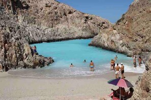 A rocky beach with clear turquoise water, people swimming and sunbathing.