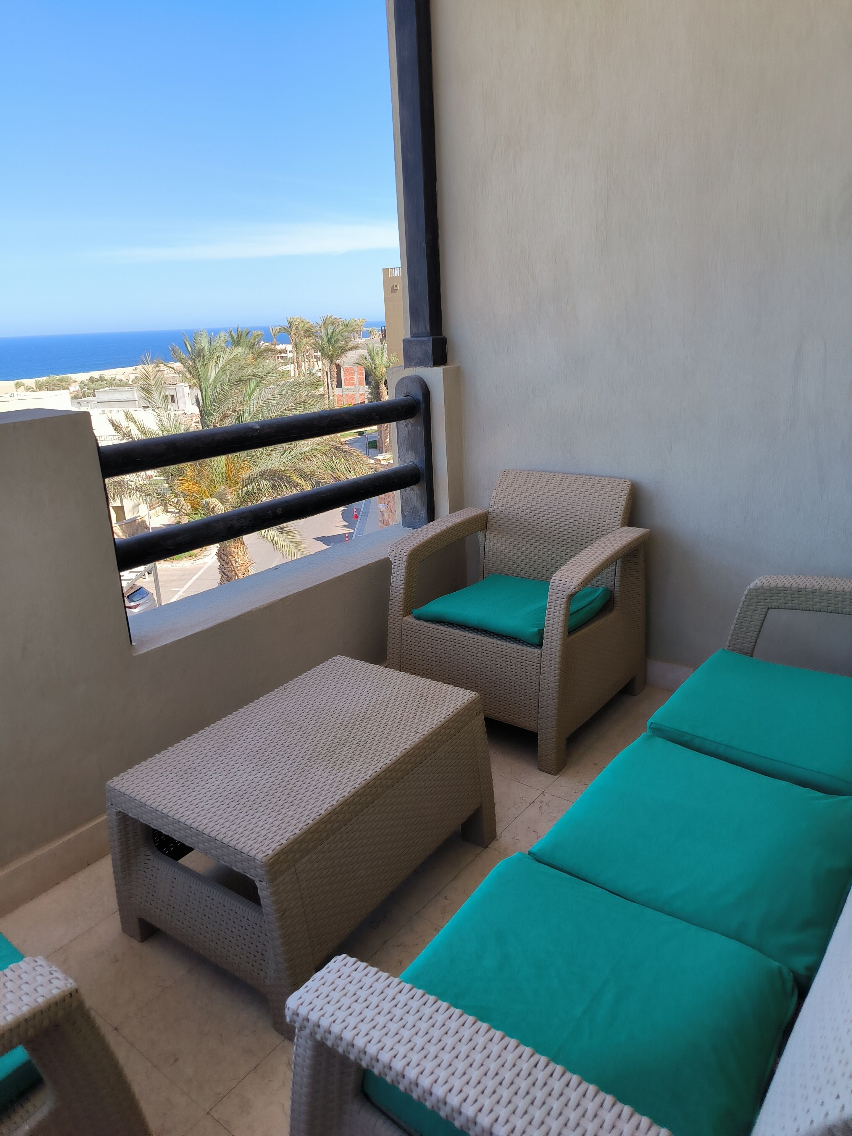 Un balcon doté de mobilier en osier, comprenant deux chaises et une petite table, offrant une vue sur la côte.