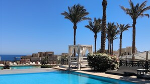 A clear blue pool with lounge chairs and palm trees, overlooking a body of water.