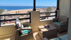 A balcony with wicker furniture and a view of the beach and ocean.