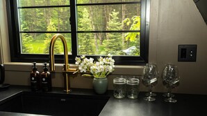 Een keuken met een zwart aanrecht, een gouden kraan, een vaas met witte bloemen en twee flessen handzeep.
