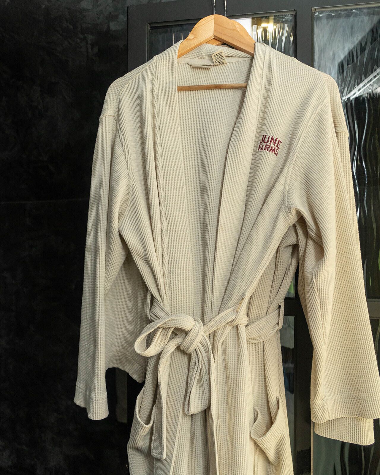 Une robe beige à taille nouée, suspendue à un cintre en bois.