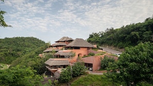 A multi-story building with thatched roofs, surrounded by lush greenery and hills.