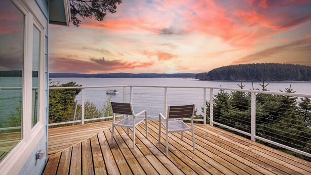 A wooden deck with two chairs overlooking a lake and forested area during sunset. - The Cliffside Poustinia (Kodiak)