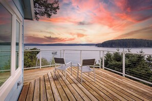 A wooden deck with two chairs overlooking a lake and forested area during sunset. - The Cliffside Poustinia (Kodiak)
