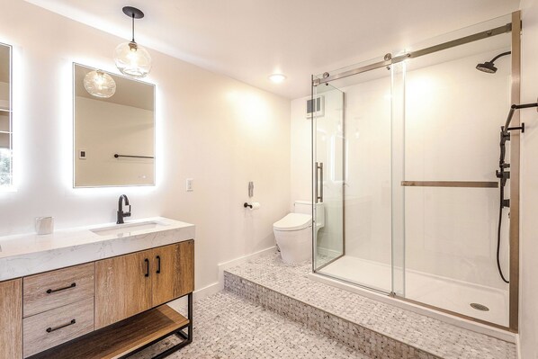 A modern bathroom with a glass-enclosed shower, a marble sink, and wooden cabinetry. - The Cliffside Poustinia (Kodiak)