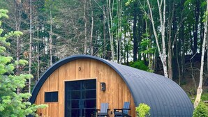 A wooden cabin with a curved roof, large windows, and a small porch area. - Treat yourself at the stunning June Farms Wellness Huts! (West Sand Lake)