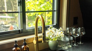 A kitchen with a gold faucet, a vase with flowers, and wine glasses on the counter. - Treat yourself at the stunning June Farms Wellness Huts! (West Sand Lake)