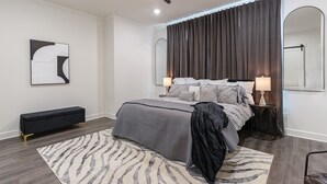 A modern bedroom with a bed, a bench, a mirror, and a ceiling fan.