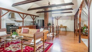 A spacious living area with a high ceiling, exposed wooden beams, a leather sofa, a coffee table, and a red patterned rug. - Sac City Loft (Sacramento)