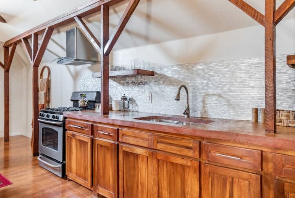 Una cocina con gabinetes de madera, una campana extractora de acero inoxidable, un horno doble y una encimera de granito.