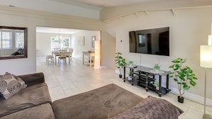 Un salon moderne avec un téléviseur à écran plat, un canapé, une table basse et un coin repas à l’arrière-plan.
