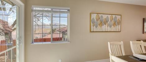 A dining area with a table and chairs, a window with a view of a mountain and a fence, and a wall-mounted artwork.