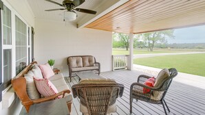 A covered porch with wicker furniture, a ceiling fan, and a view of a grassy field. - Beautiful Georgia Farmhouse Rental w/ Patio (Lenox)