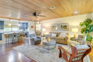 A spacious living area with a wooden ceiling, a kitchen in the background, and a dining area with bar stools.