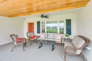 A covered porch with wicker furniture, a ceiling fan, and a view of a green field through windows.