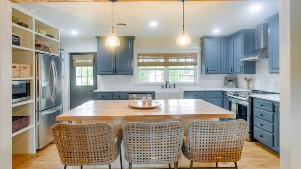 A modern kitchen with a central island, three wicker chairs, and built-in appliances. - Beautiful Georgia Farmhouse Rental w/ Patio (Lenox)