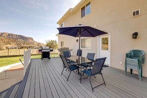 Een terras buiten met een barbecue, een eettafel, stoelen en een parasol.