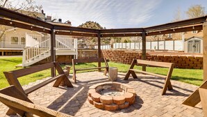 Un espacio al aire libre con un pozo de fuego, bancos de madera y una estructura de pérgola.