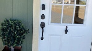 Une porte blanche avec une fenêtre, une petite plante en pot et un sonnette.