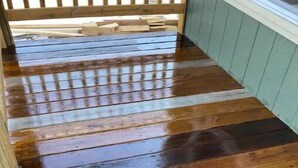 Une terrasse en bois avec une rambarde en bois et un mur de couleur vert clair.