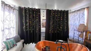 A room with a large bathtub, a white sofa, and curtains with string lights.