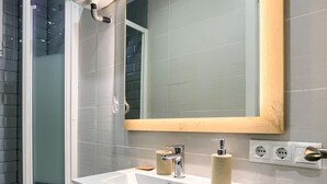 Un bany modern amb un rentapeus blanc, un mirall amb estructura de fusta i una zona de dutxa.